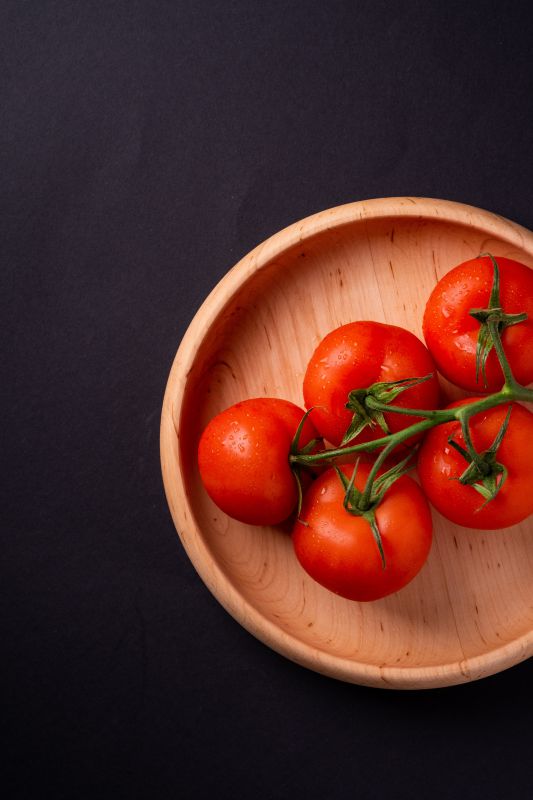 Five red tomatoes in a wooden bowl.